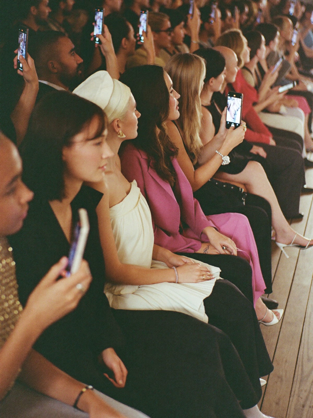 Front row at a runway show, phones raised